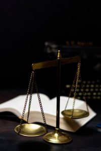 Representação do conceito de justiça e equilíbrio com uma balança dourada, um livro aberto e uma máquina de escrever ao fundo, evocando temas de direito e conhecimento.